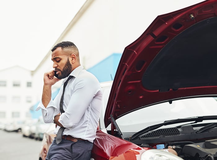 Person on phone next to car with hood raised.