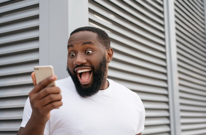 Young man makes a surprised happy face at his phone.