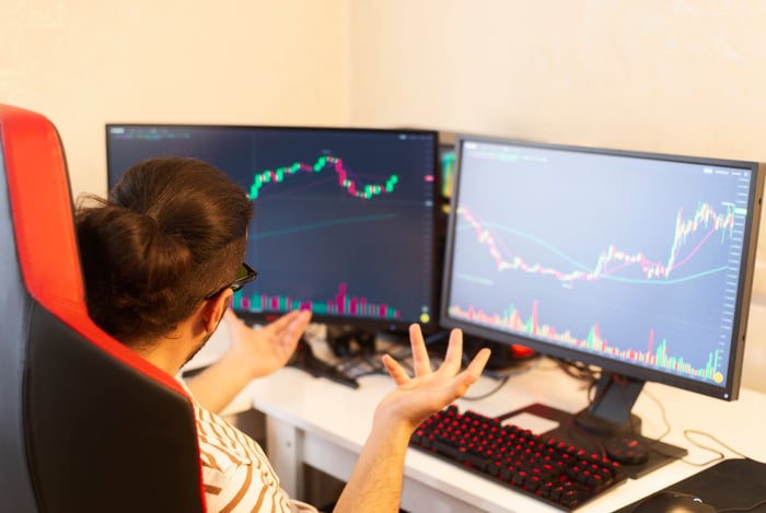 An investor looking at stock charts on their computer monitors with confusion.