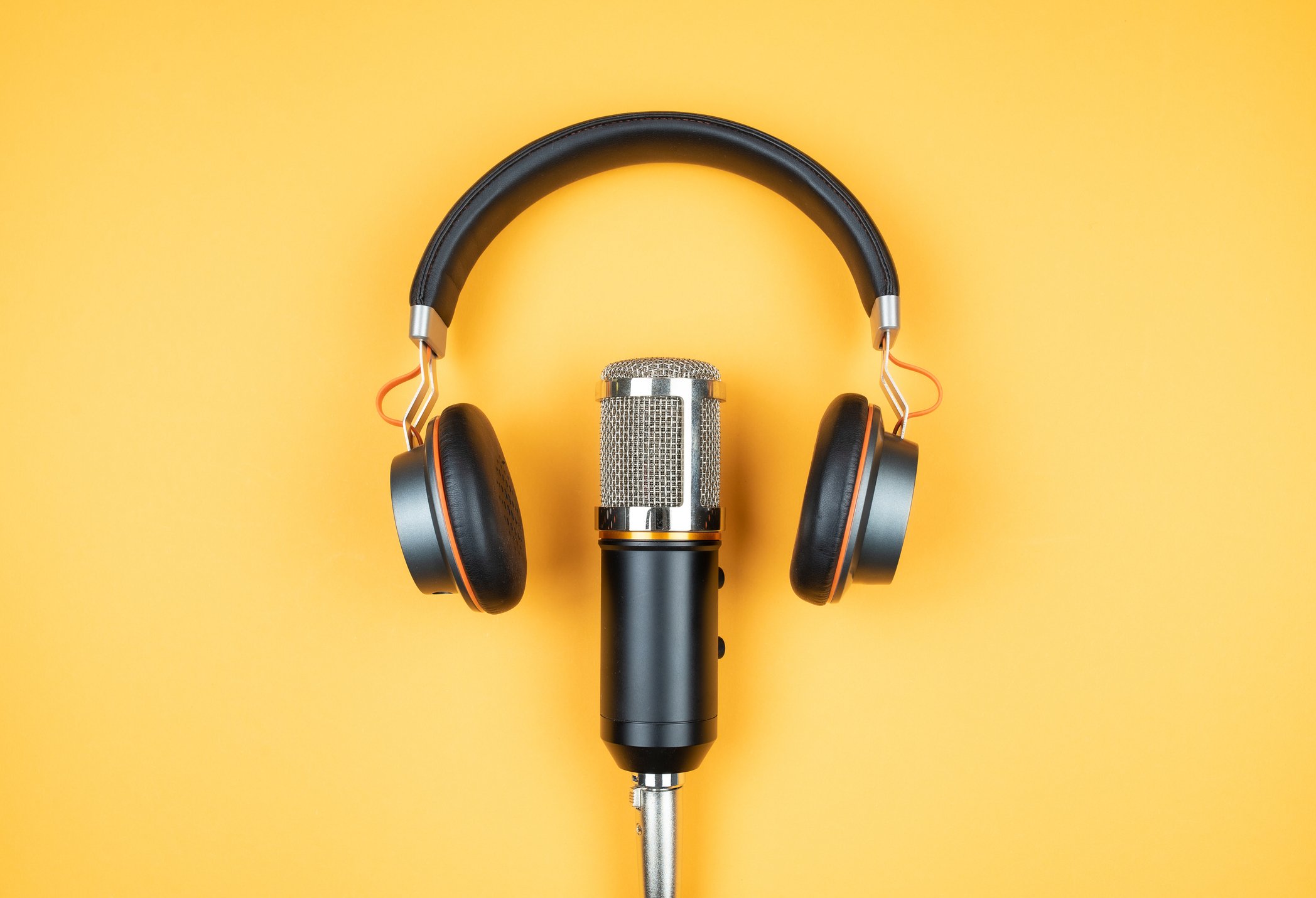 Podcast microphone and earphones on a yellow background.