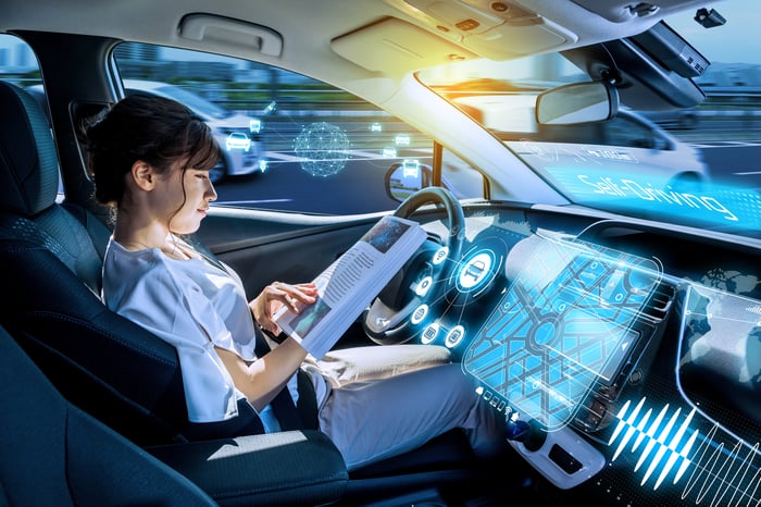 A person reading a book in the driver's seat of a self-driving car.