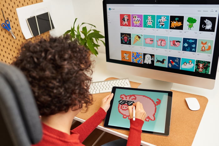 A creator designs an image on a tablet with many more displayed on a computer.