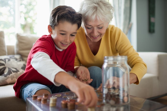 An older person counting coins with a younger person and putting them in a jar.