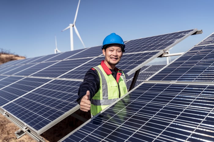 Smiling construction worker gives a thumbs up in the middle of a field of solar panels.