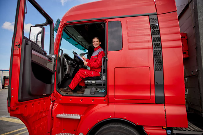 Woman in red uniform sitting at the wheel of a big red tractor trailer semi truck.