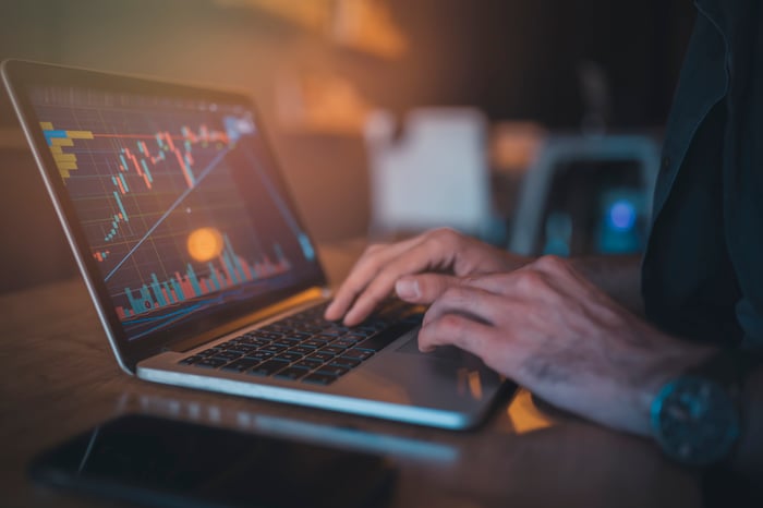 A person typing on a laptop that's displaying a rising crypto chart with an uptrending line.