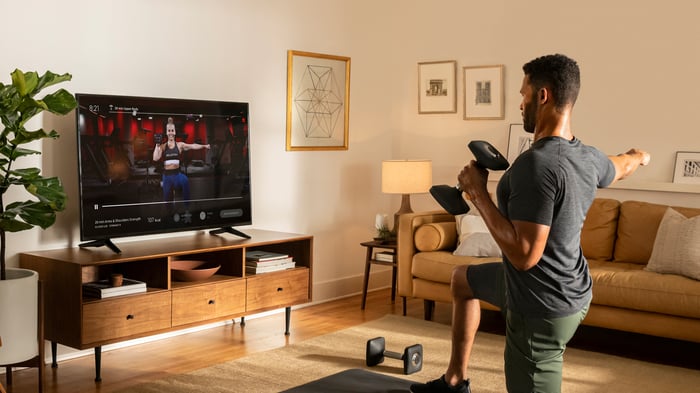 A person holding a weight and looking at a screen with a fitness instructor.