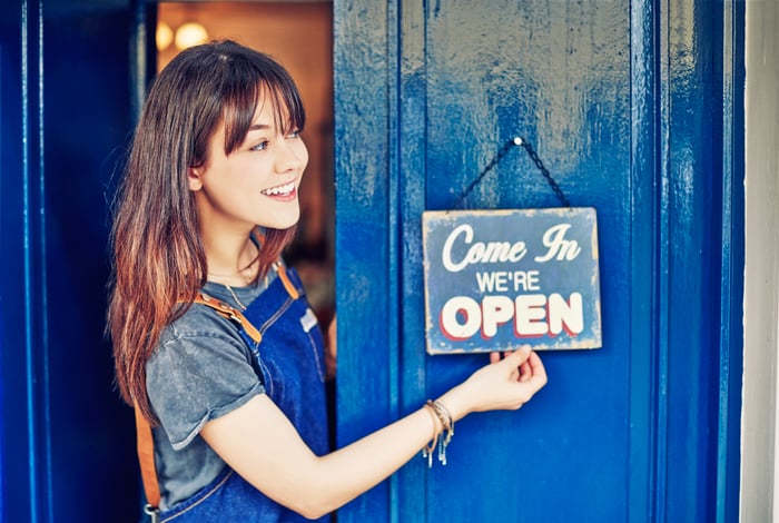 Smiling business owner hanging open sign on shop door.