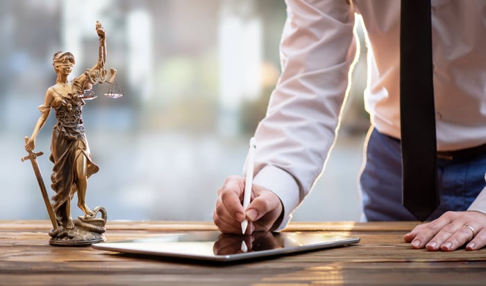 A person signing a digital tablet on a table next to a Lady Justice figurine.