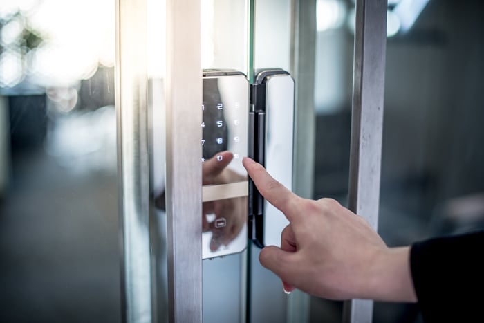 A person's outstretched hand entering a code on a building entry keypad.