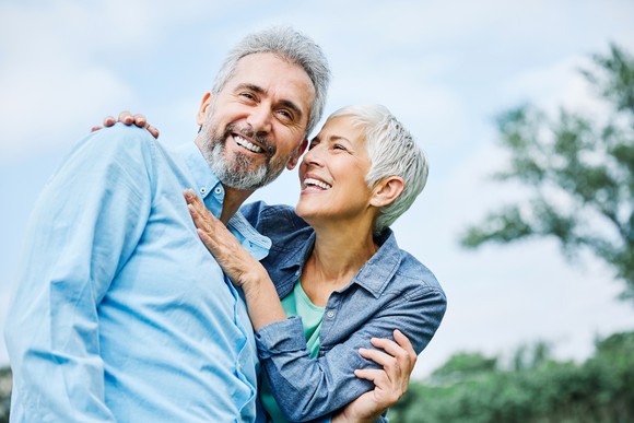 Two smiling people embracing outdoors.