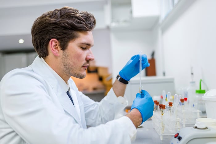 A scientist manipulates a genetic sample in a test tube while sitting at a laboratory bench.
