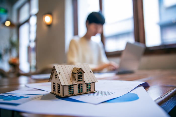 A real estate agent on a laptop with a miniature house in focus.