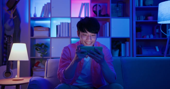 Person playing a mobile game on their phone in a dimly lit room.