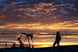 A person looking at an oil pump with the sun setting in the background.