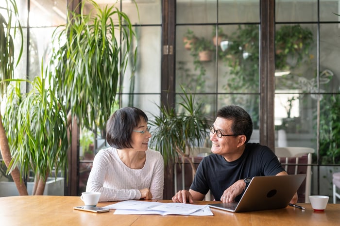 People smiling at each other in front of laptop in dining room.