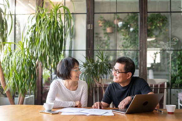 People smiling at each other in front of laptop in dining room.