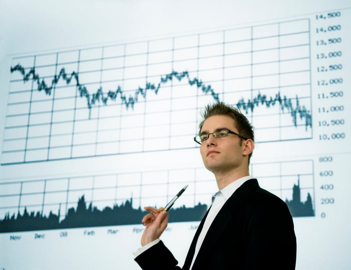 A person in a suit points to a declining stock chart.