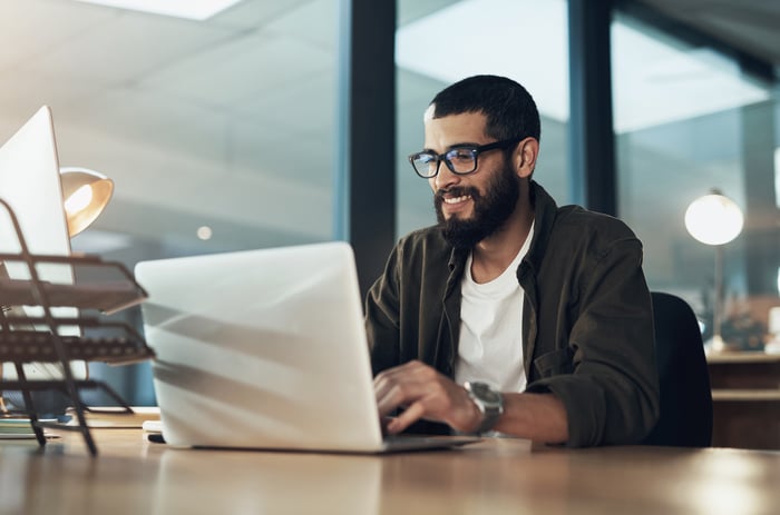 A smiling person at a laptop.