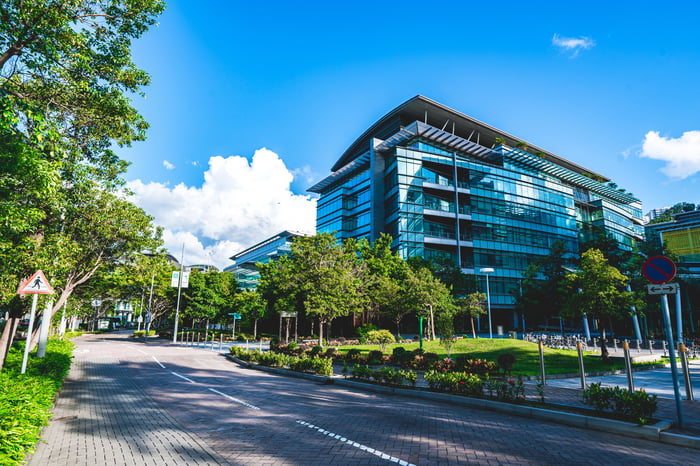 A commerical real estate building against a bright blue sky and clouds next to a tree-lined street.