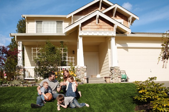People in front yard of single family home playing with ball on grass.
