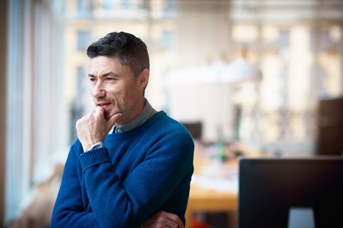 A person standing and pondering a decision while looking out the window.