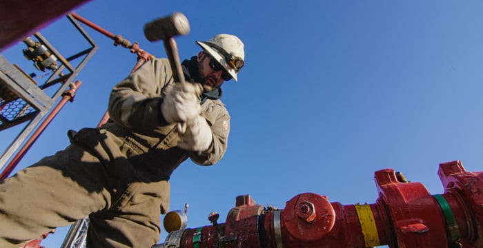 A person holding a hammer next to a natural gas well.