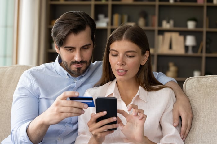 A young couple keying credit card information into a smartphone screen.