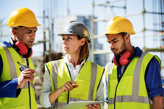 Three construction workers using a tablet on the job site.