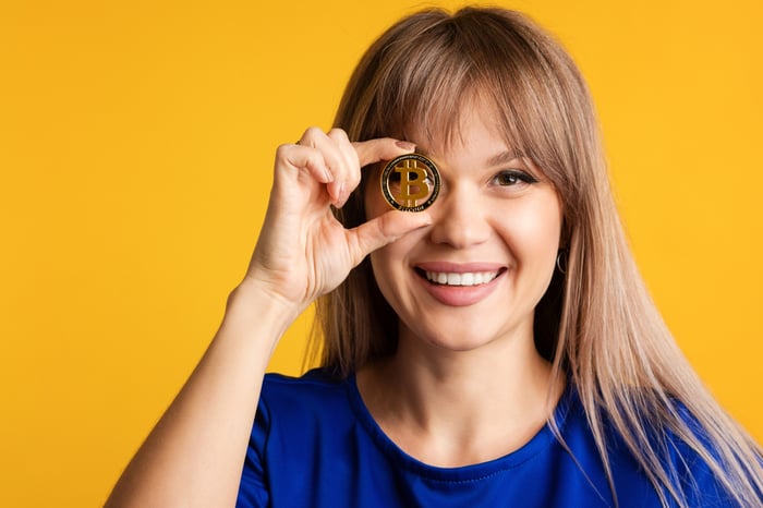 Lady holding a bitcoin up to her eye like a monacle.