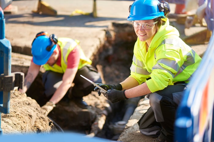Workers laboring in, and next to, an open trench.