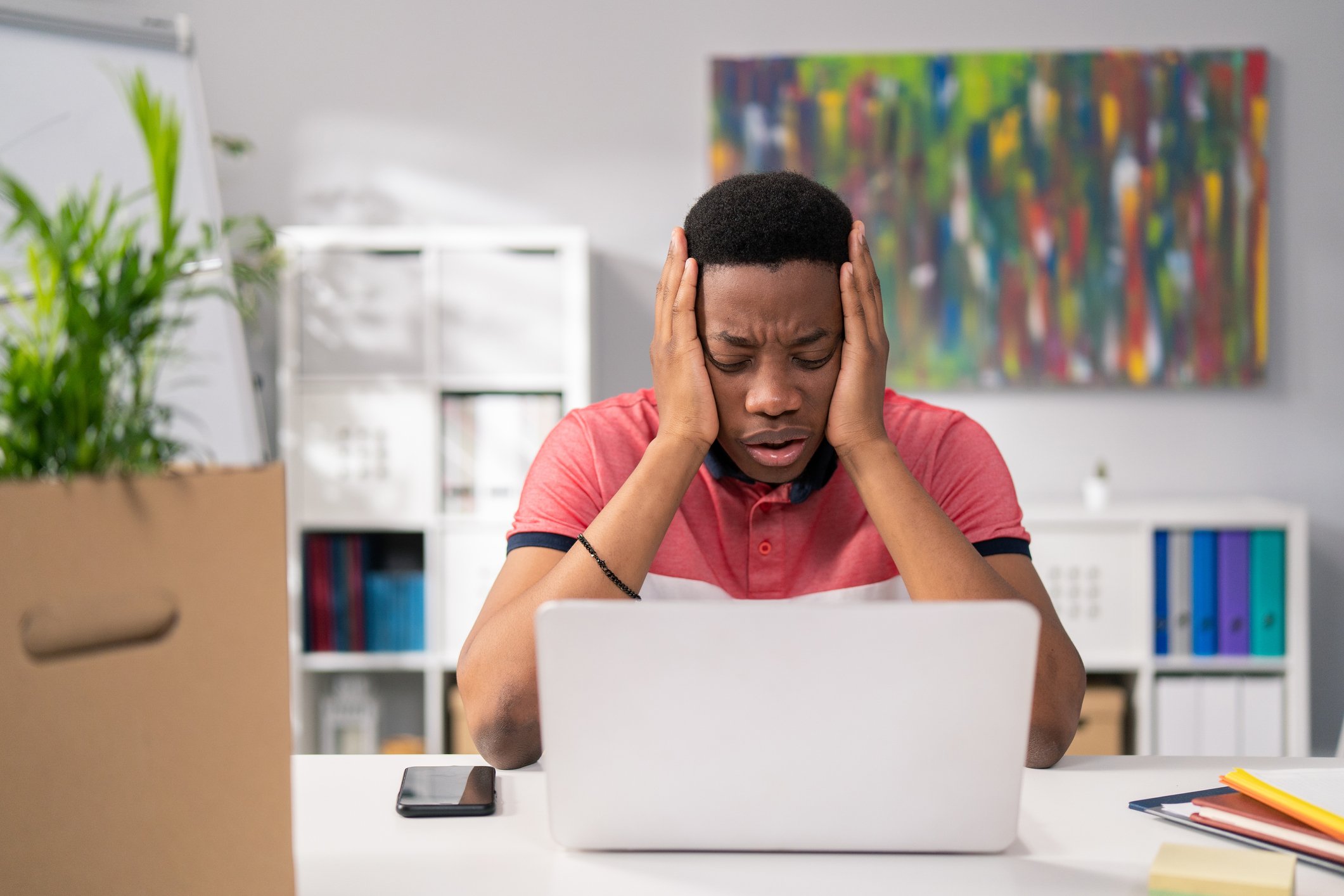 A concerned man holds his head while looking at his laptop.