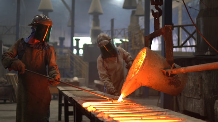 Two people pouring molten aluminum into forms.