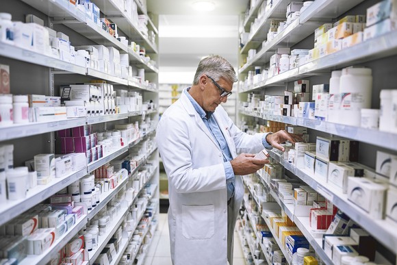 A pharmacist looks at drugs on a shelf.
