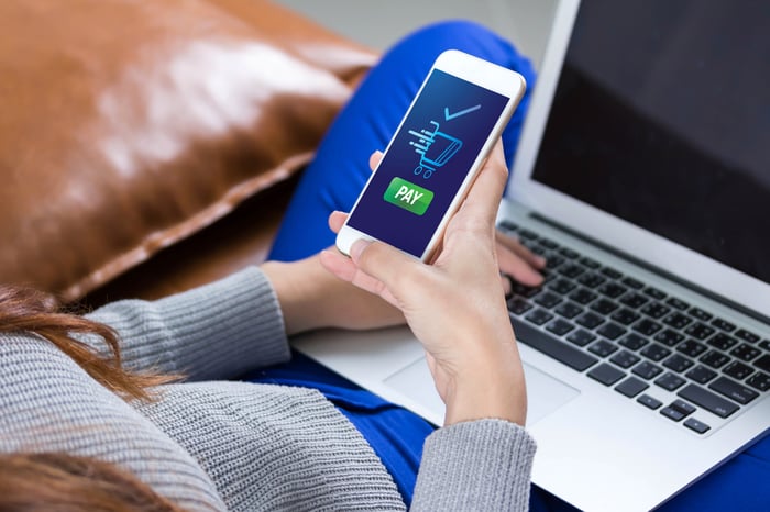 Person using an iPhone while sitting with a Macbook on their lap.