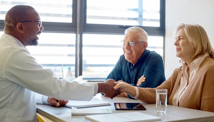 Two people sitting across a desk from another person and shaking hands.