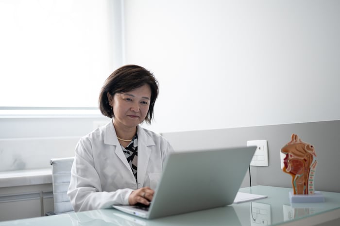 A doctor smiles while conducting a telehealth visit on a laptop.