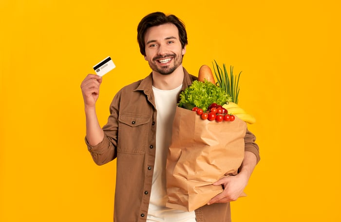 Person holding payment card and grocery bag.