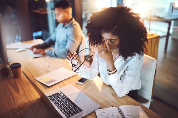 Stressed person pinching bridge of nose while seated at a laptop.