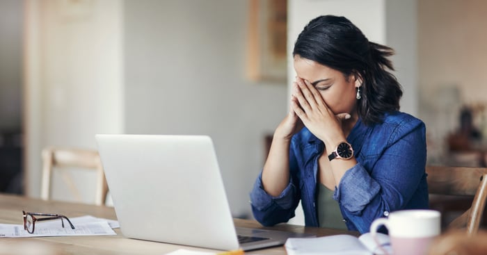 A person at a laptop covering their face.