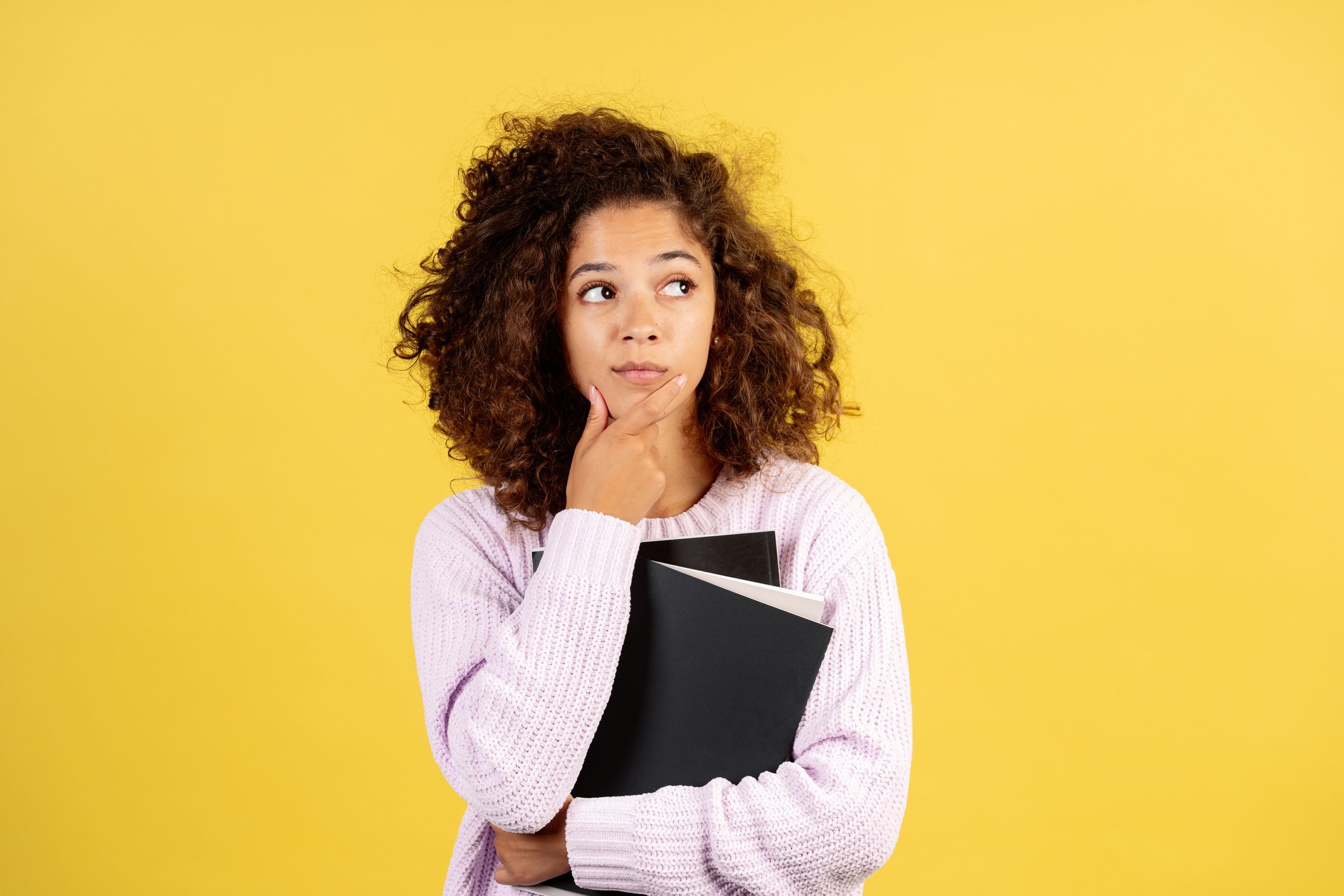 A woman holds notebooks while holding her chin in thought.