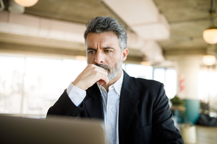 A person wearing professional attire with a serious expression at a laptop.