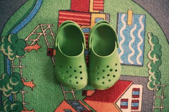 Pair of green foam clog shoes on top of a carpet.