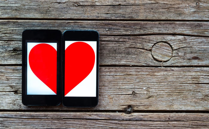 The shape of a heart is displayed across two side-by-side mobile phones set against rough wooden boards.