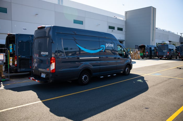A dark-colored Amazon Prime van parked outside a fulfillment center.