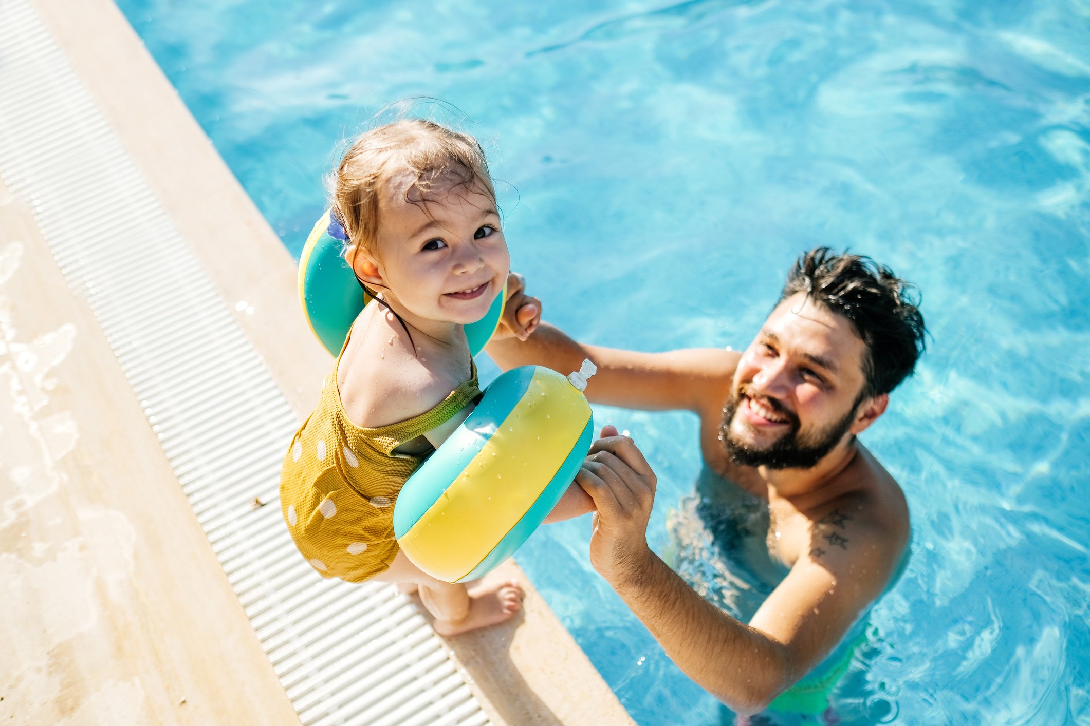 Father and baby daughter playing in a swimming pool.