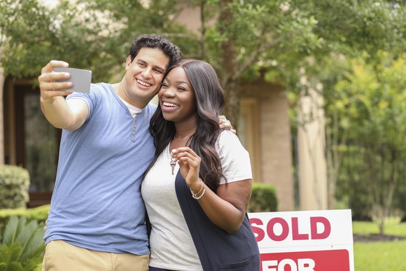 Excited couple standing in front of a "sold" sign.