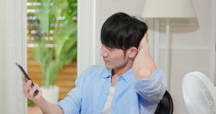 Young man scratches his head looking at his phone.