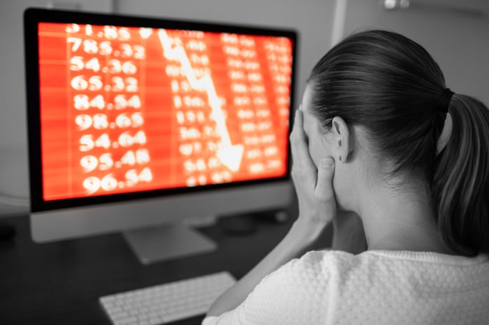 A person holding face in front of a computer showing stock losses.