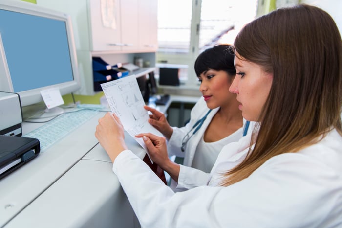 Two scientists consider a printout detailing genomic data while standing at a computer in a laboratory.